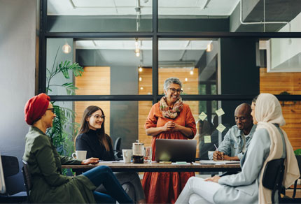 Five diverse individuals sitting around a table in a meeting room, engaged in conversation.
