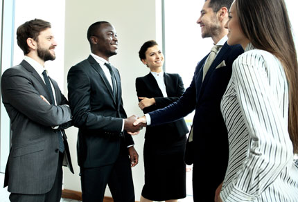Group of business people surrounding two people shaking hands.