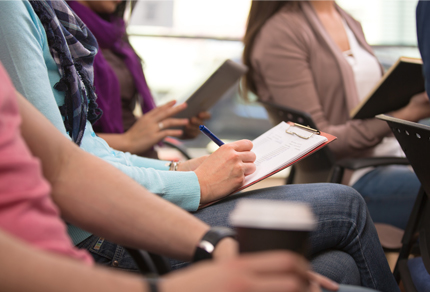 Close up of a student's hands taking notes on a clipboard.