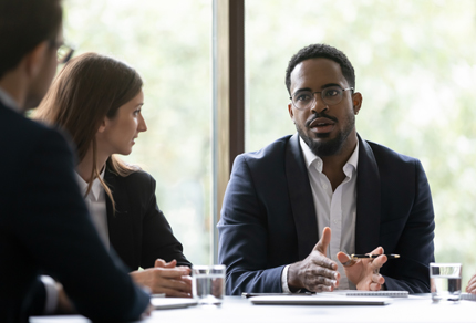 A man talking to two colleagues while seated at a table.