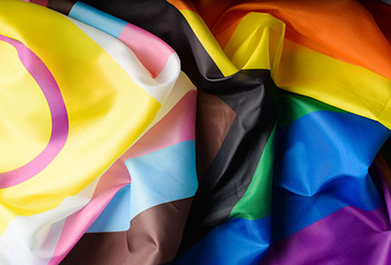 Progress pride flag waving in the wind against a blue sky
